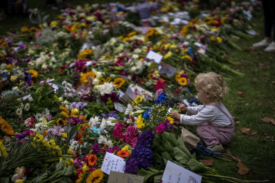 A child crouches down to touch flowers, next to a broad pile of bouquets.