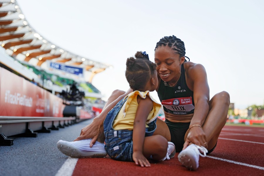 Athlete Allyson Felix sits closely to her young daughter on a track.