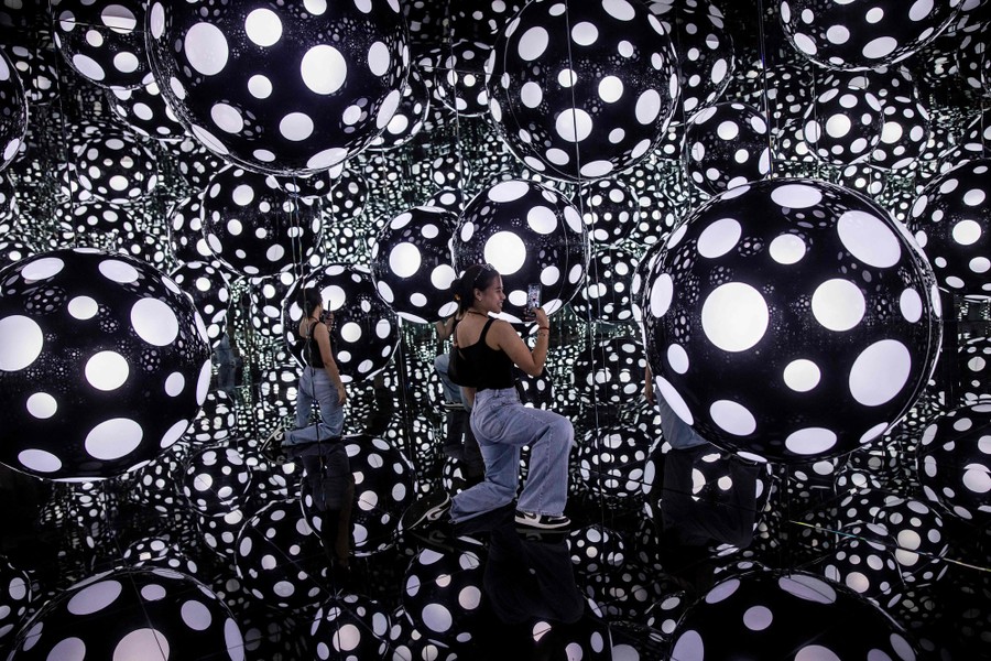 A person takes a photo inside a mirrored room filled with many large polka-dot balls.