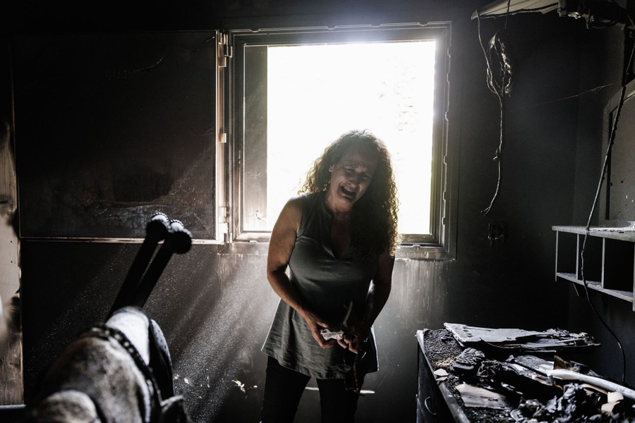 Μια γυναίκα κλαίει ενώ στέκεται μέσα σε ένα καμένο σπίτι.