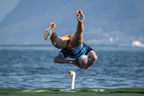 A rugby player leaps from a floating pitch into a lake; a swan in the distance appears to be right under him.