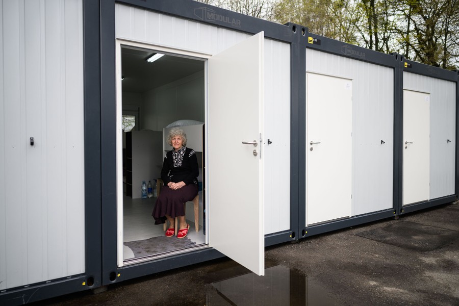 A woman sits in the open doorway of a modest shelter built from a shipping container.