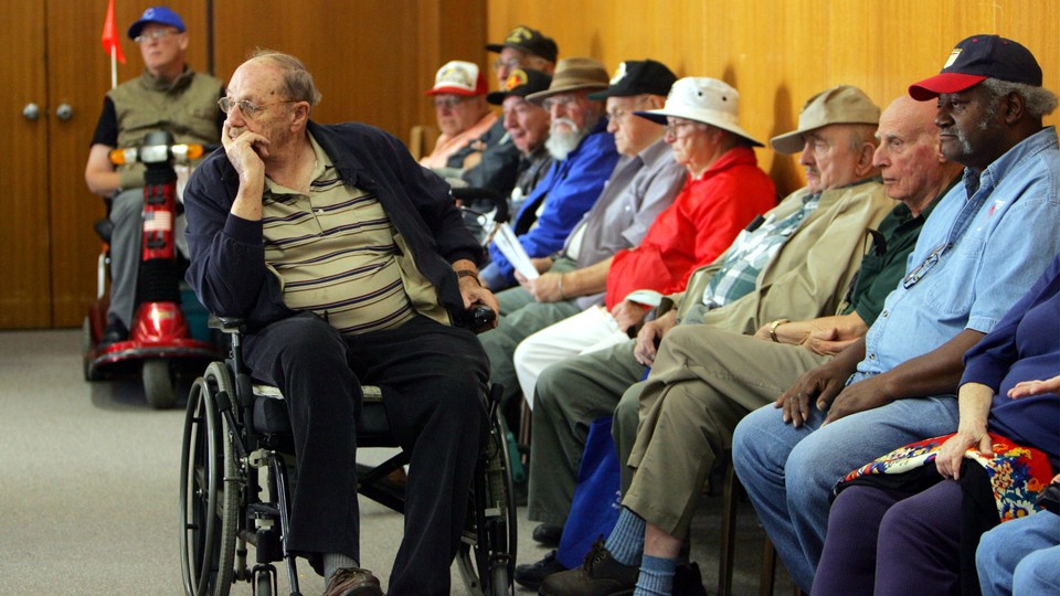 Older people wait in chairs and wheelchairs.