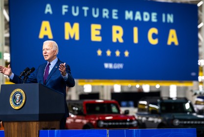 Joe Biden at a podium, with electric cars in the background behind him