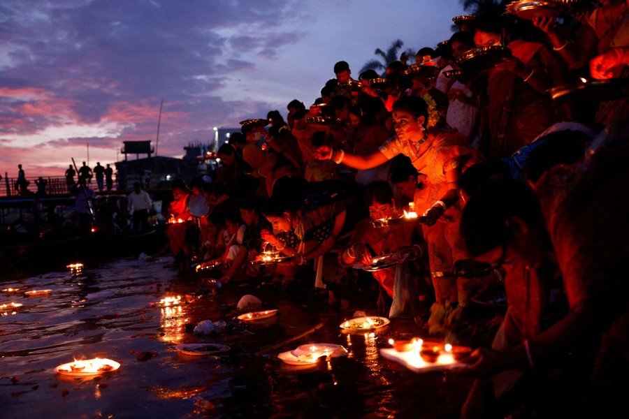 Dozens of people kneel to set oil lamps afloat on a river.