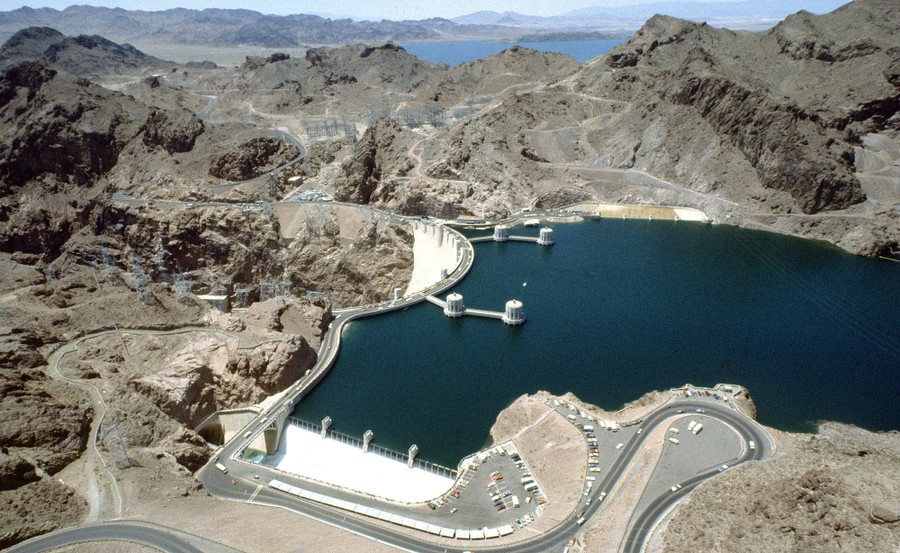 An aerial image of a very full reservoir behind a dam, surrounded by arid, rocky terrain.