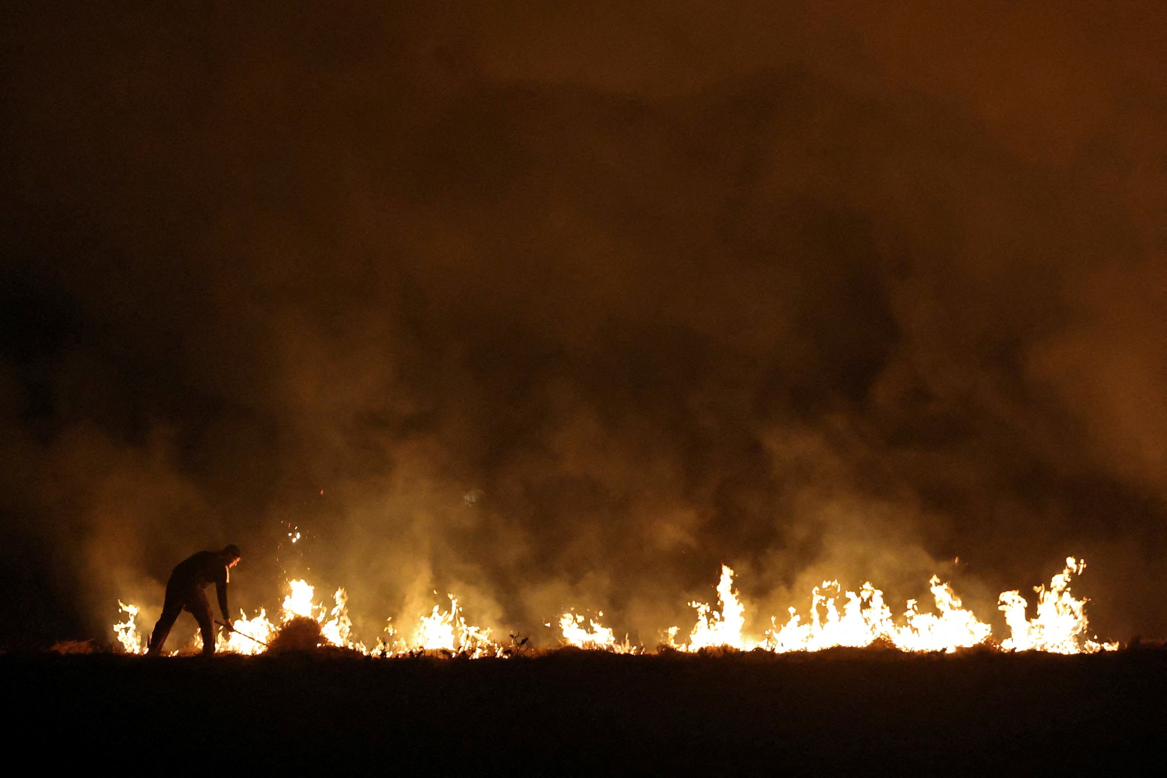 A farmer burns stubble in a field, seen at night.