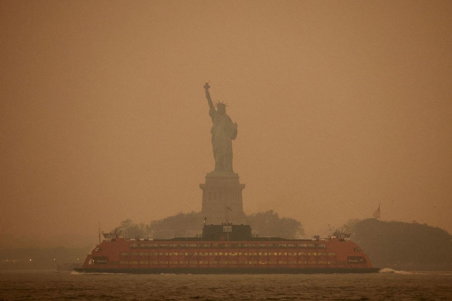 A ferry passes the Statue of Liberty in a hazy sky.
