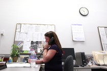 A woman uses an office phone at a desk.