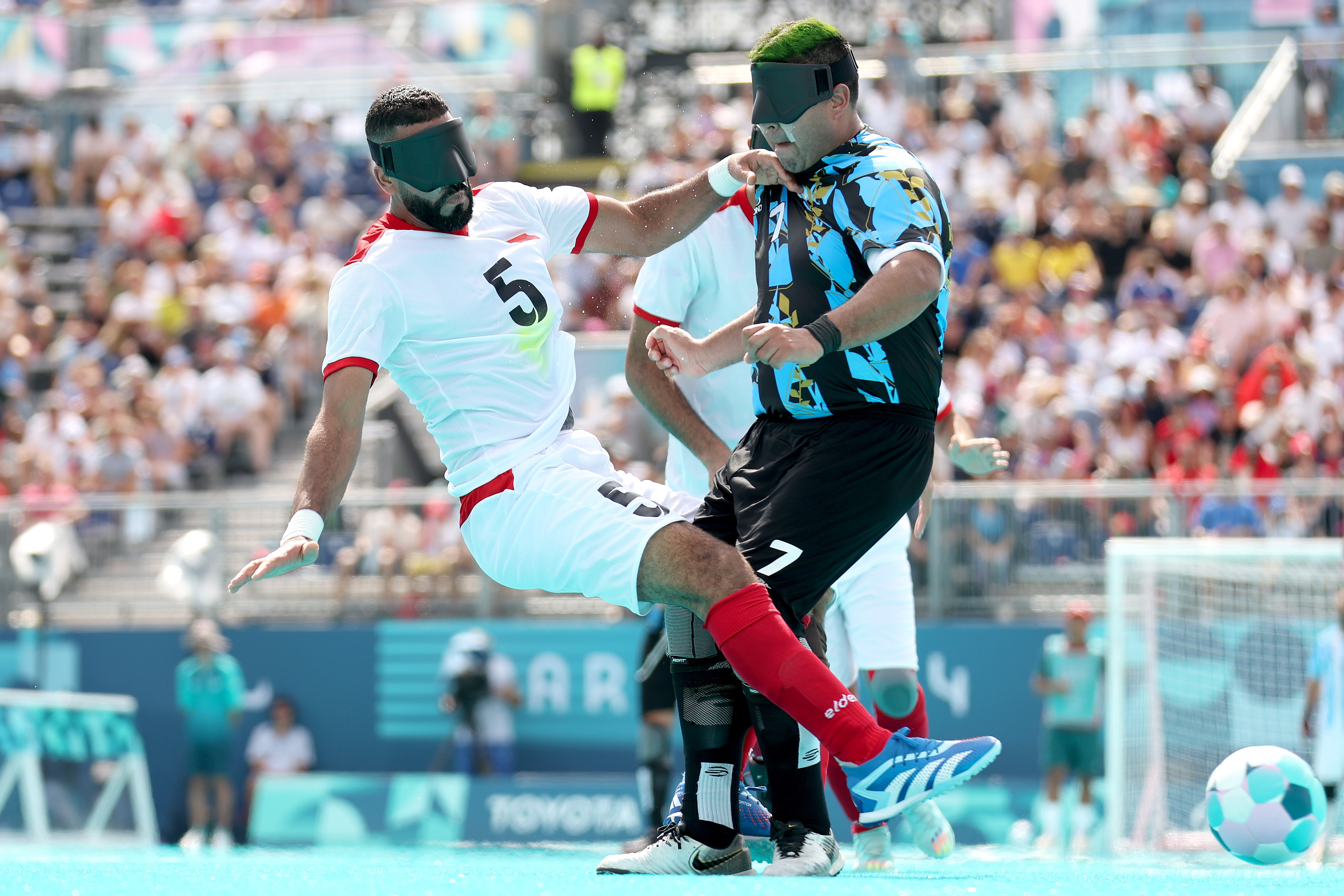 Two football players wearing blindfolds collide while chasing the ball during a match at the Paralympic Games.