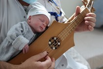 A newborn child rests on the chest of a person playing a traditional stringed instrument.