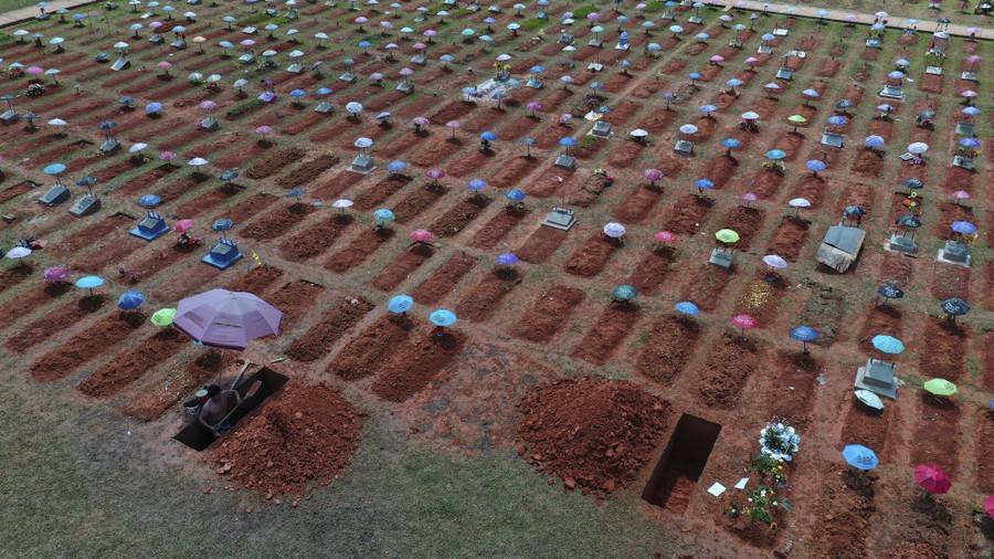A worker digs a new grave beside hundreds of other recently filled graves in a cemetery.