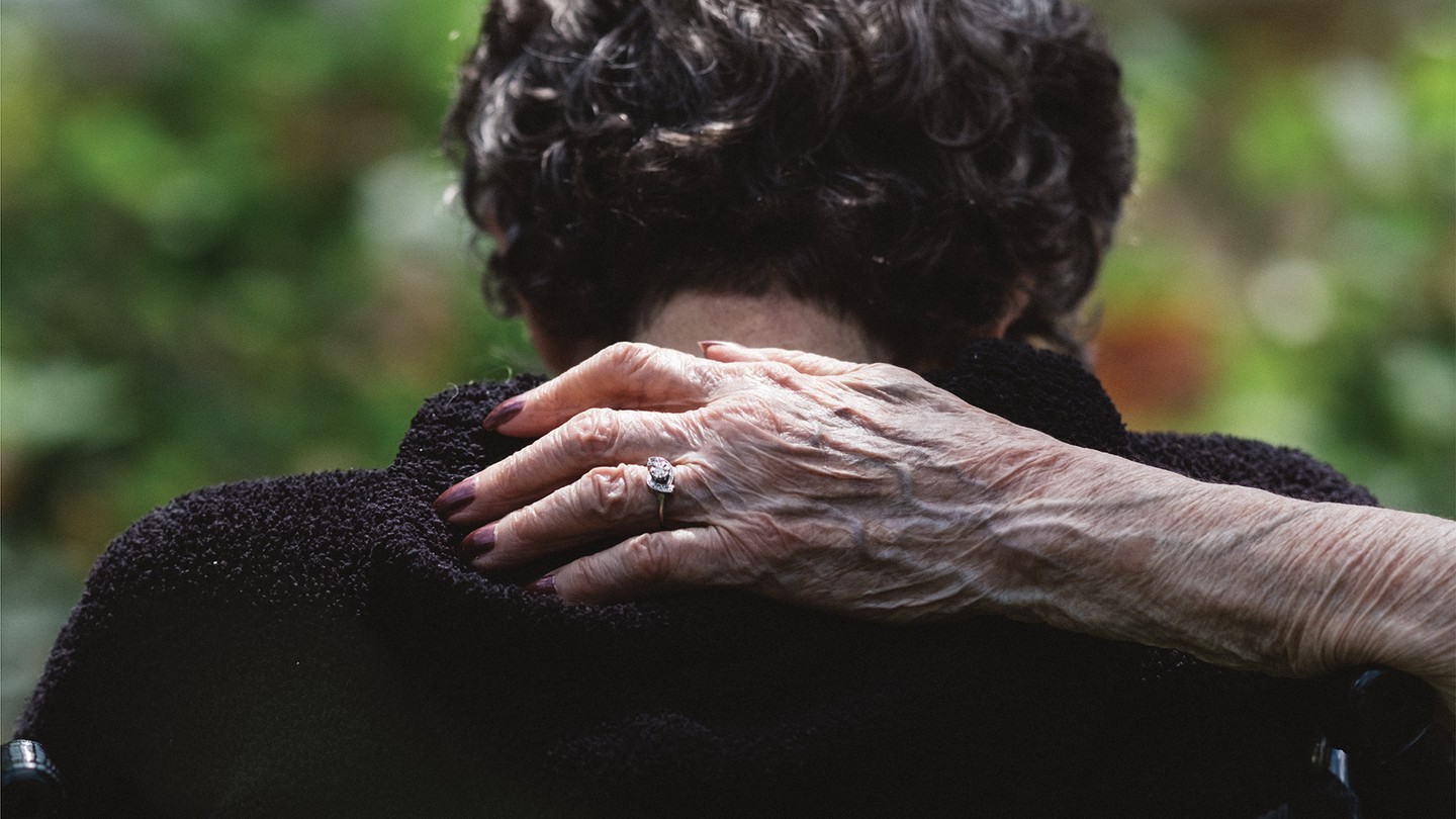 a hand wearing an engagement ring pats the back of an older woman