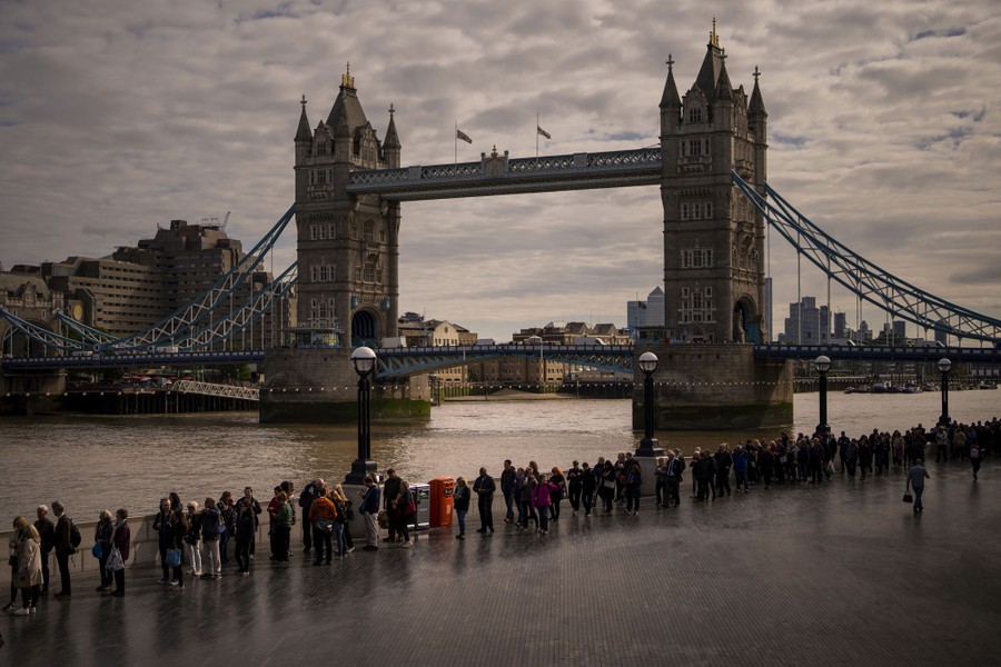 A long line of people stand beside the Thames River at London's Tower Bridge.