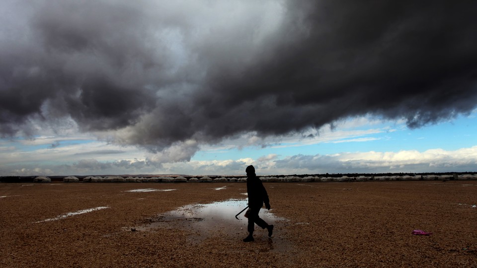 A Syrian refugee walks toward his tent at Zaatari refugee camp through puddles and in front of storm clouds.