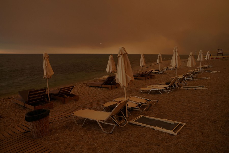 Smoke fills the sky above a beach lined with empty beach chairs.
