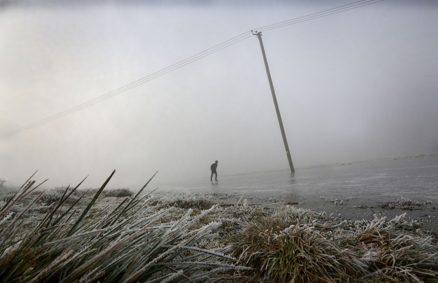 A person skates across a frozen fen on a foggy day.