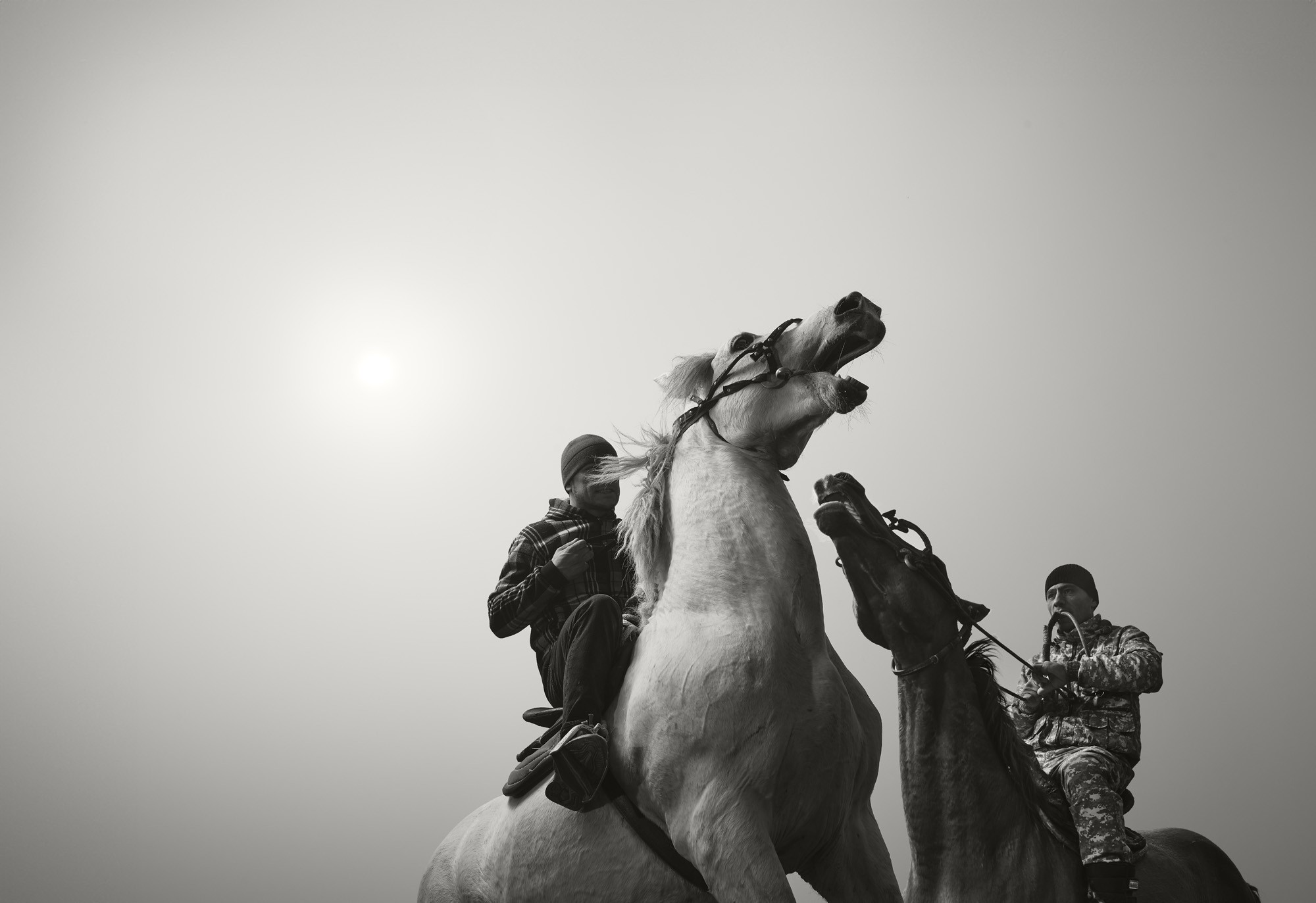 Two people, seen on horseback, against a gray sky.