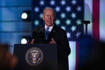 Biden with an animated expression giving a speech in front of a flag