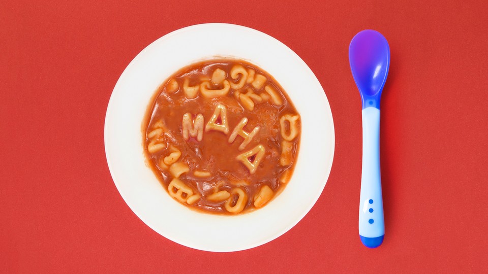 A bowl of tomato soup in which noodles spell out "MAHA," next to a blue plastic spoon
