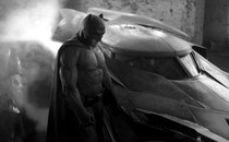 Black-and-white photo of Ben Affleck playing Batman, standing next to the Batmobile