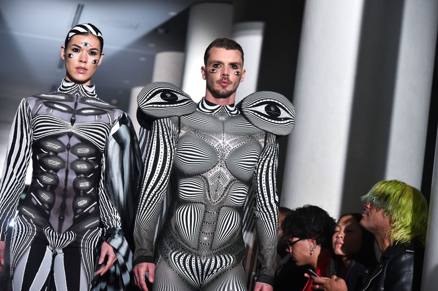 Two models wear unique and complex black-and-white striped garments on a runway.