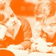 Two kids read a book together in the grass