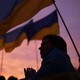 A crowd waving Ukrainian flags in front of sunset sky.