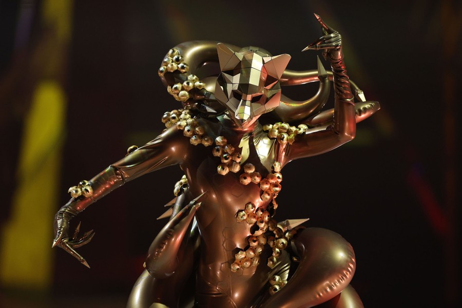 A model displays an intricate full-body costume with a faceted fox-shaped mask.