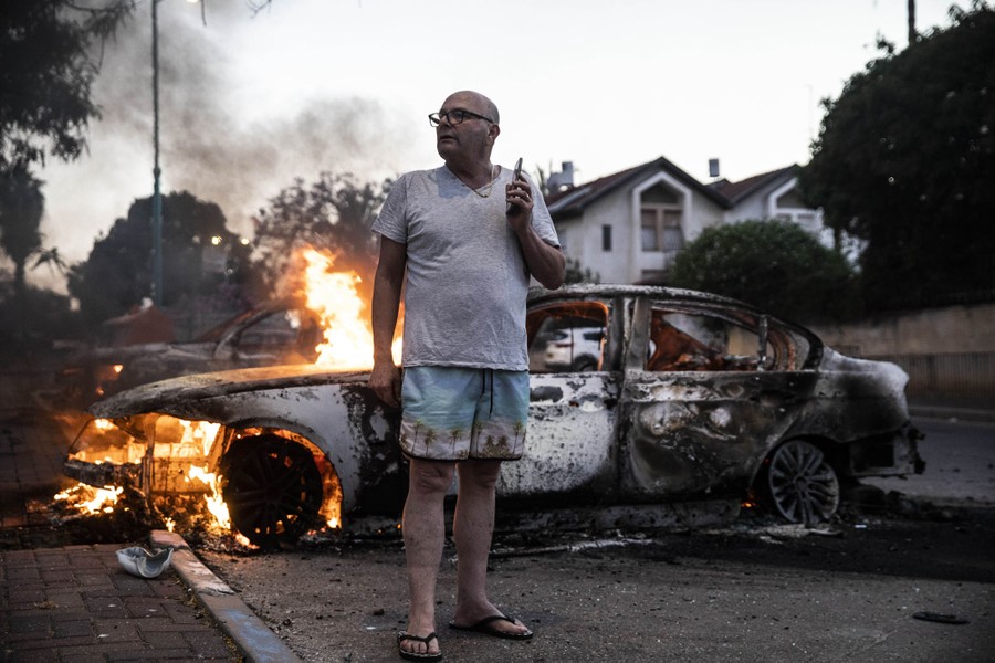 A man stands beside a burning car.