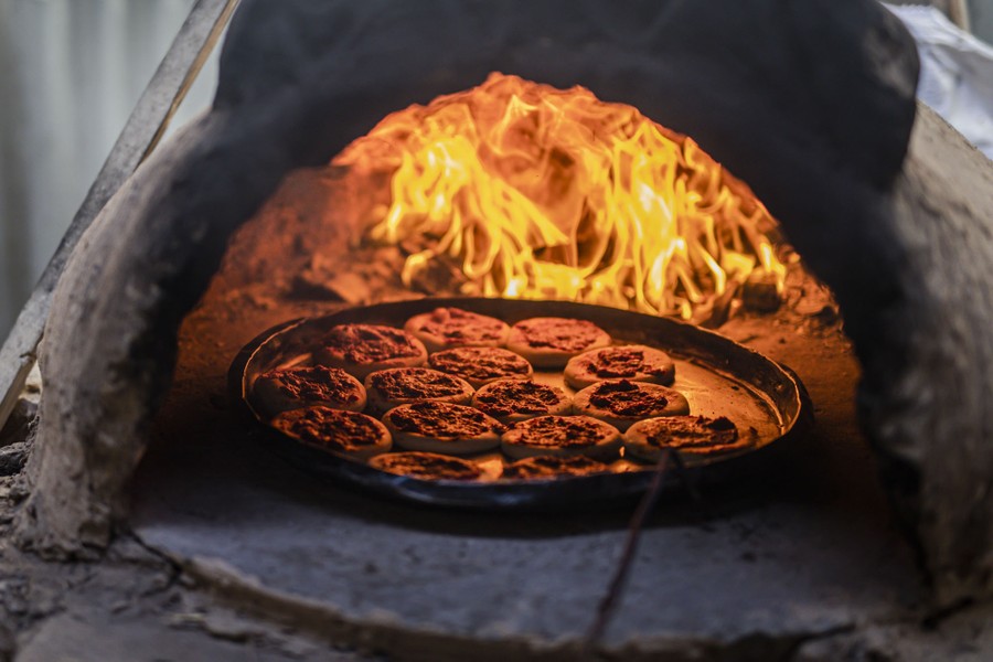 A platter of food cooks inside a wood-fire oven.