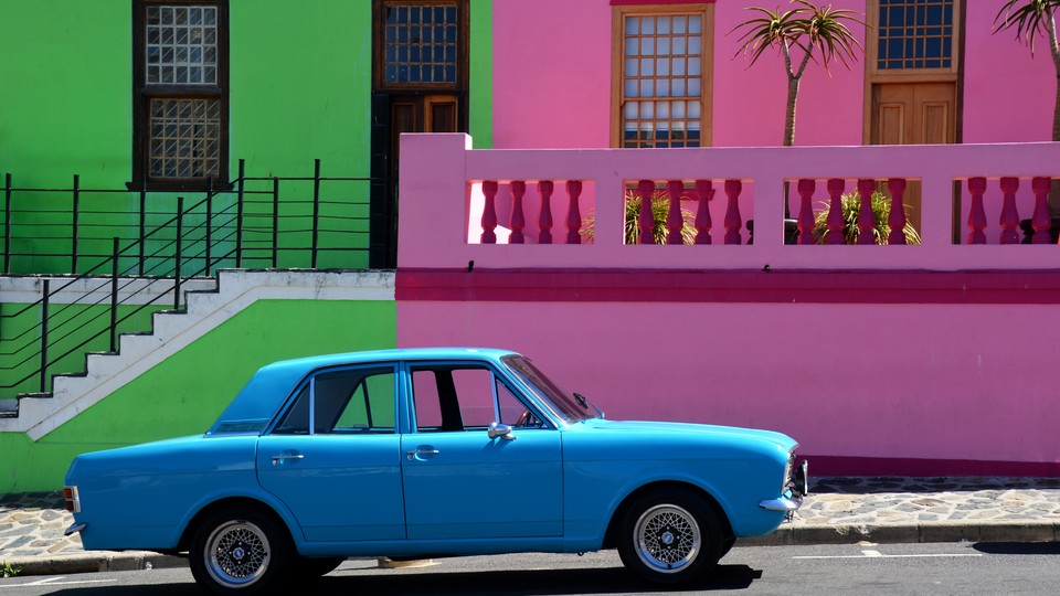 A bright blue car parked in front of pastel pink and green buildings