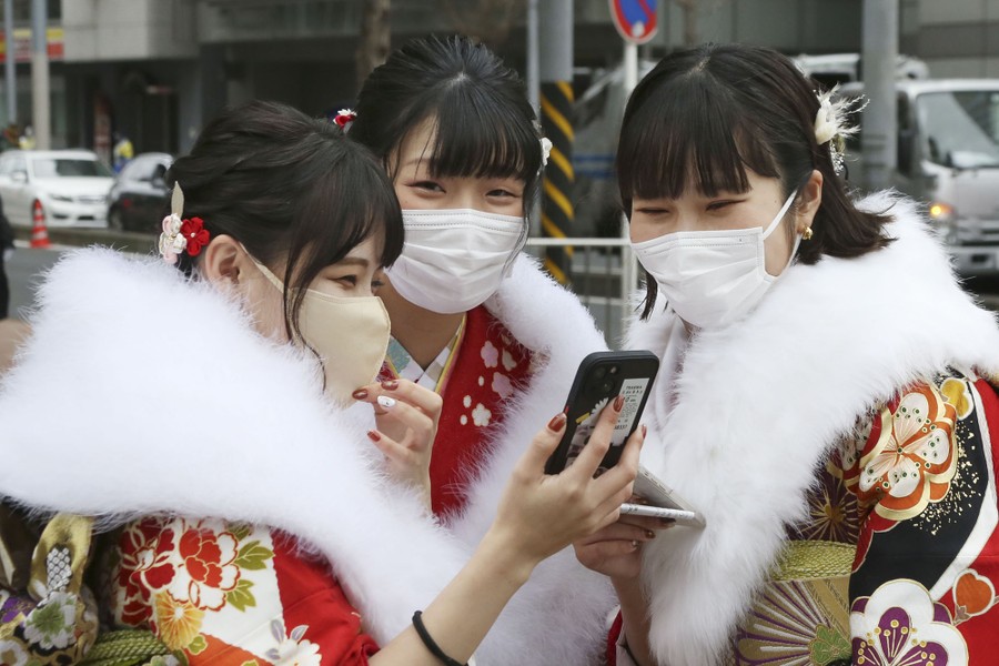 Three young women in traditional clothing take selfies in a street.