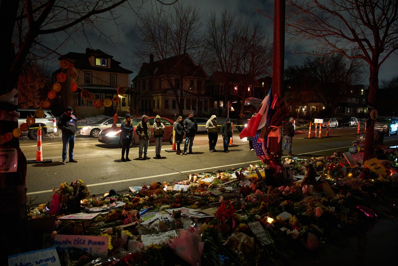People standing in a residential street at night visit a makeshift memorial for Renee Good.