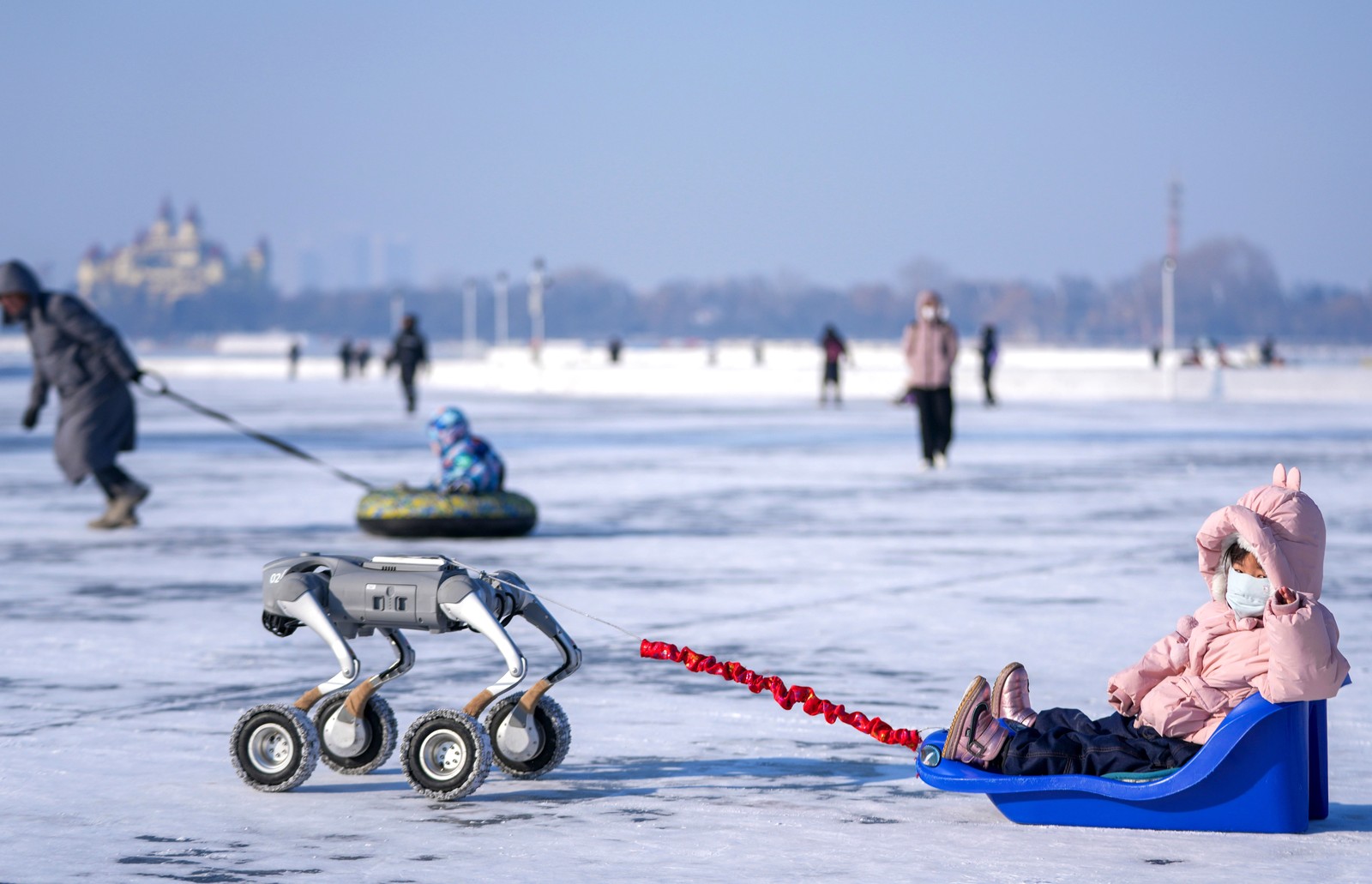 A child rides sled pulled by a wheeled robot on the frozen surface of a river.