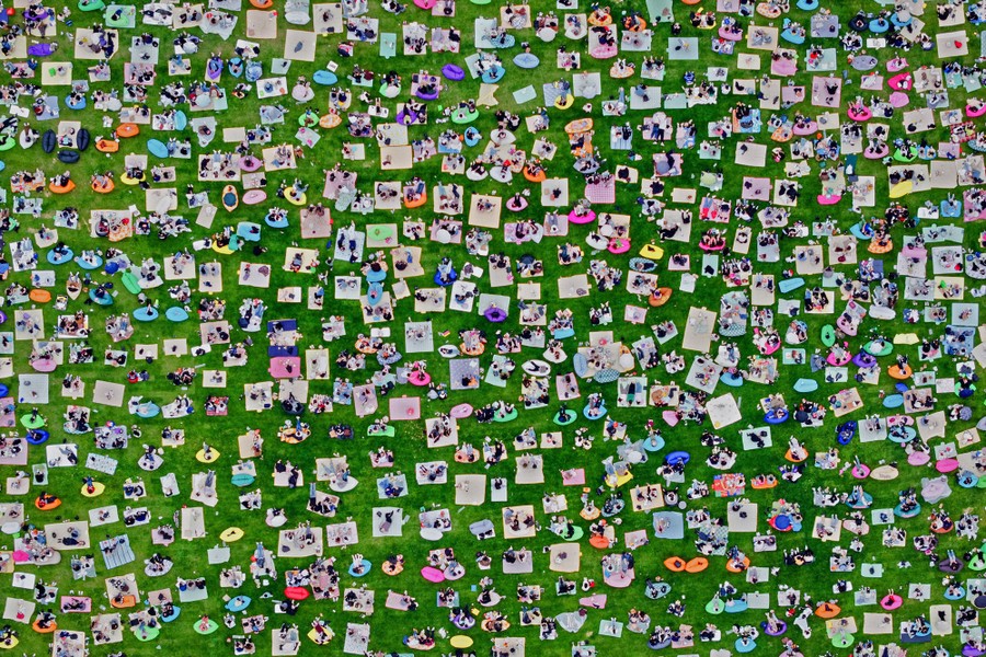An aerial view of hundreds of blankets arranged on grass with several people on each blanket