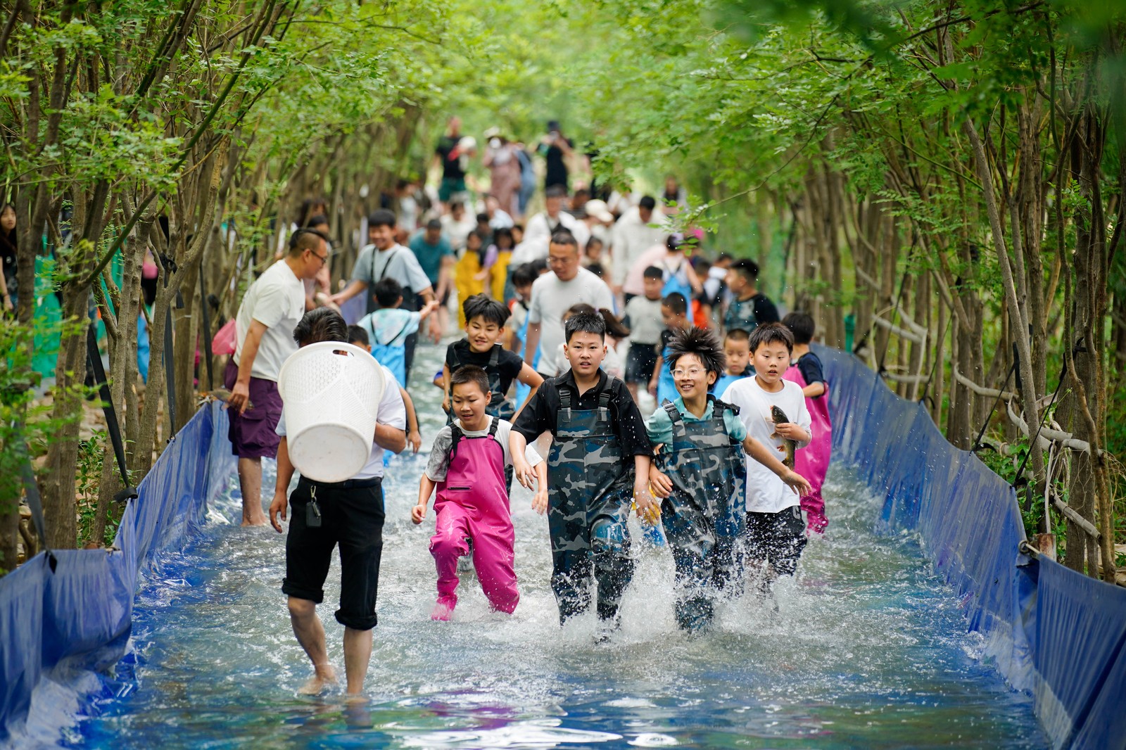 Children and parents playfully splash while walking on a path turned into a long wading pool.