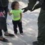 A small child looks at a border patrol agent as she and an adult, both asylum seekers, are taken into custody.