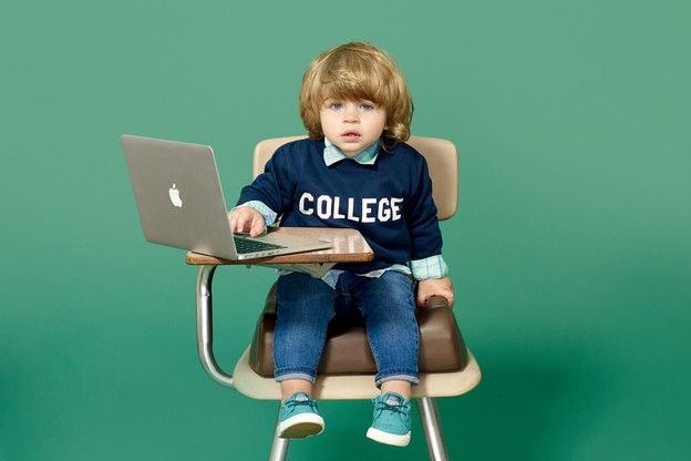 Small child in a desk chair with a laptop, dressed in a collegiate sweatshirt