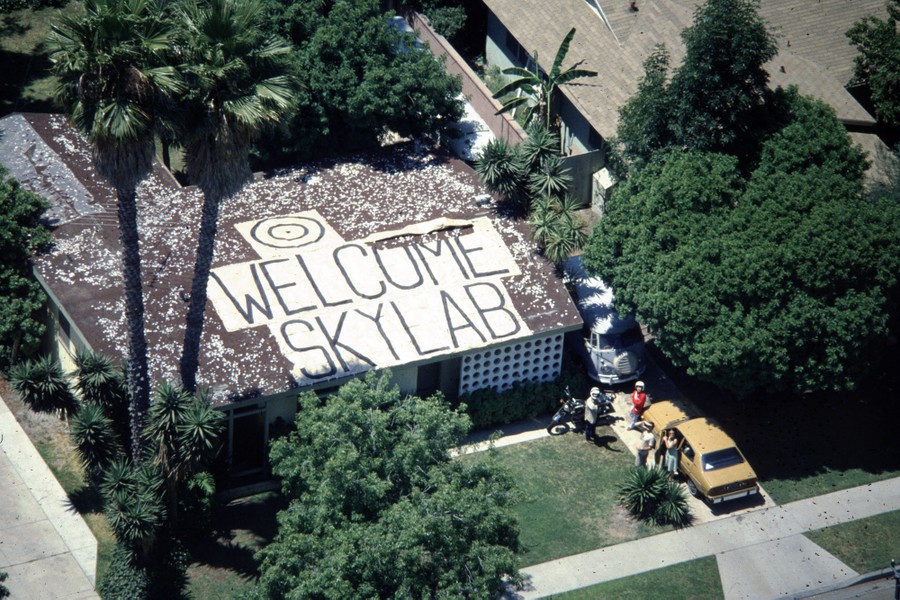 An aerial view of a suburban house with a handmade sign on the roof featuring a bull's-eye and the words 