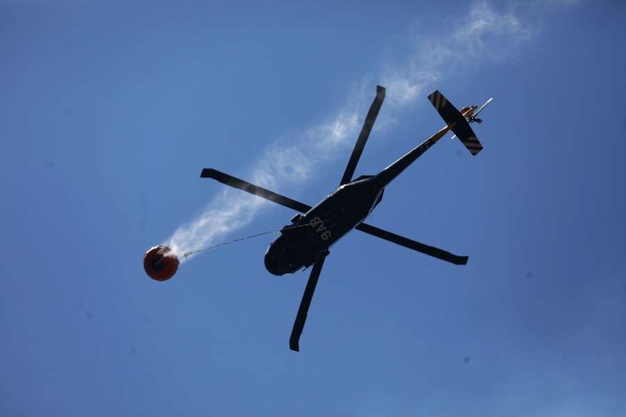 A helicopter carries water in a large bucket.