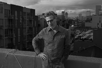 BW image of a man on a rooftop looking at the camera with his hand on his hip