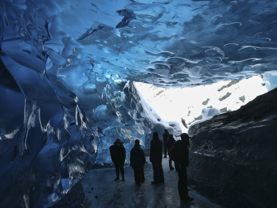 Several people walk in an ice cave near the entrance.