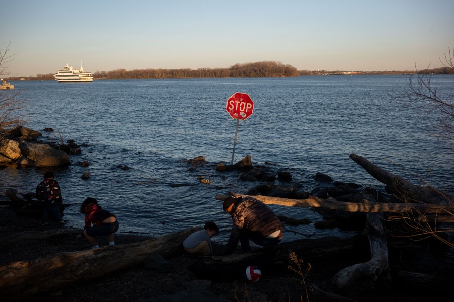 Children play along the a river, beside a stop sign that has been oddly placed on the shore.