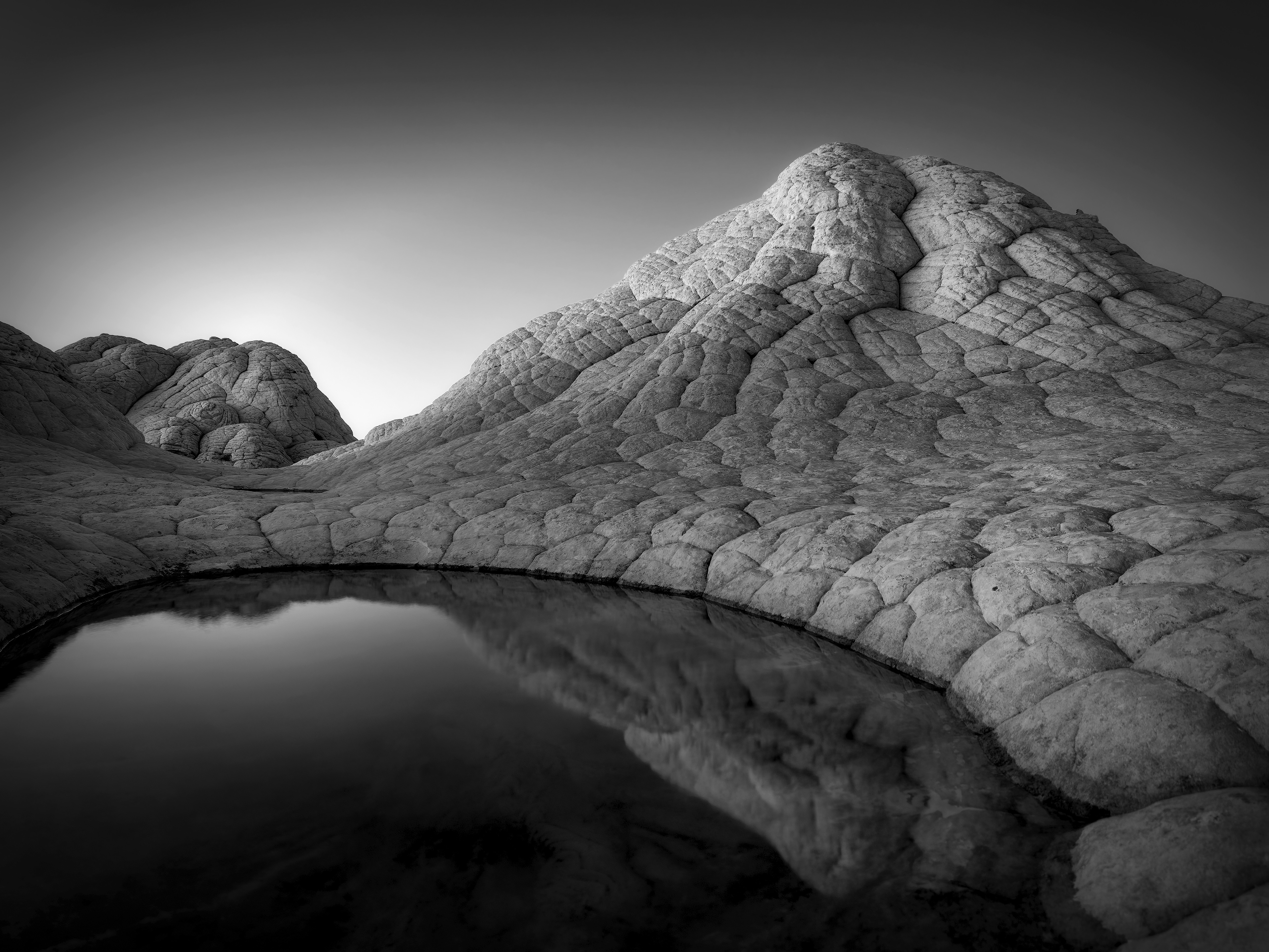 A black-and-white view of a cracked and weather-worn rock outcrop beside a small body of water