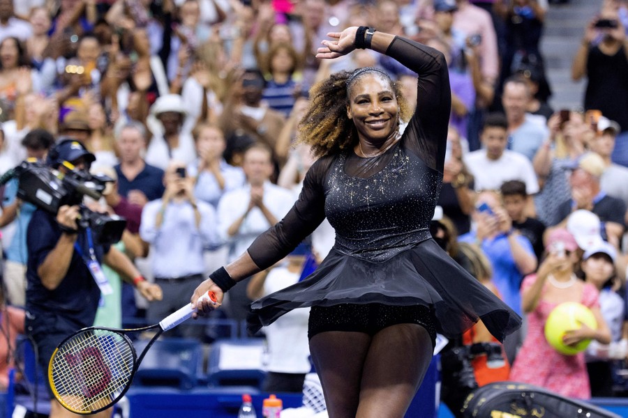 Serena Williams raises her arm and celebrates on the court, in front of a large cheering crowd.