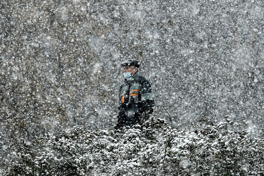 A man wearing a face mask walks during heavy snowfall.