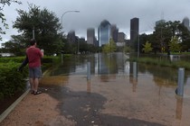 A man stands in a flooded city park, with Houston's skyline in the background