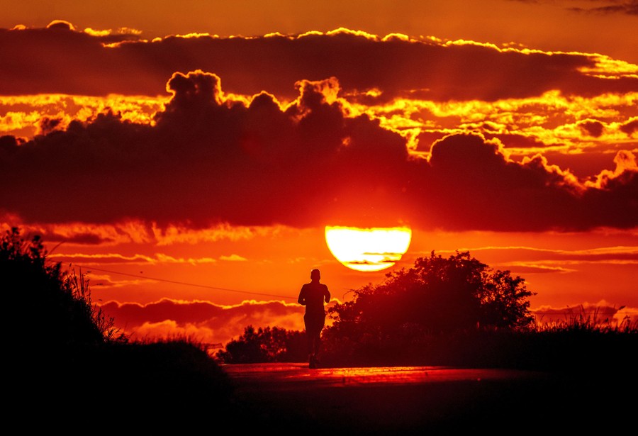 A man runs along a small road as the sun rises.