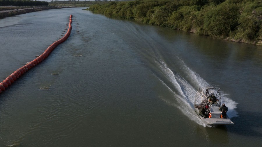 An air boat moves along a river, past a long string of floating buoys.